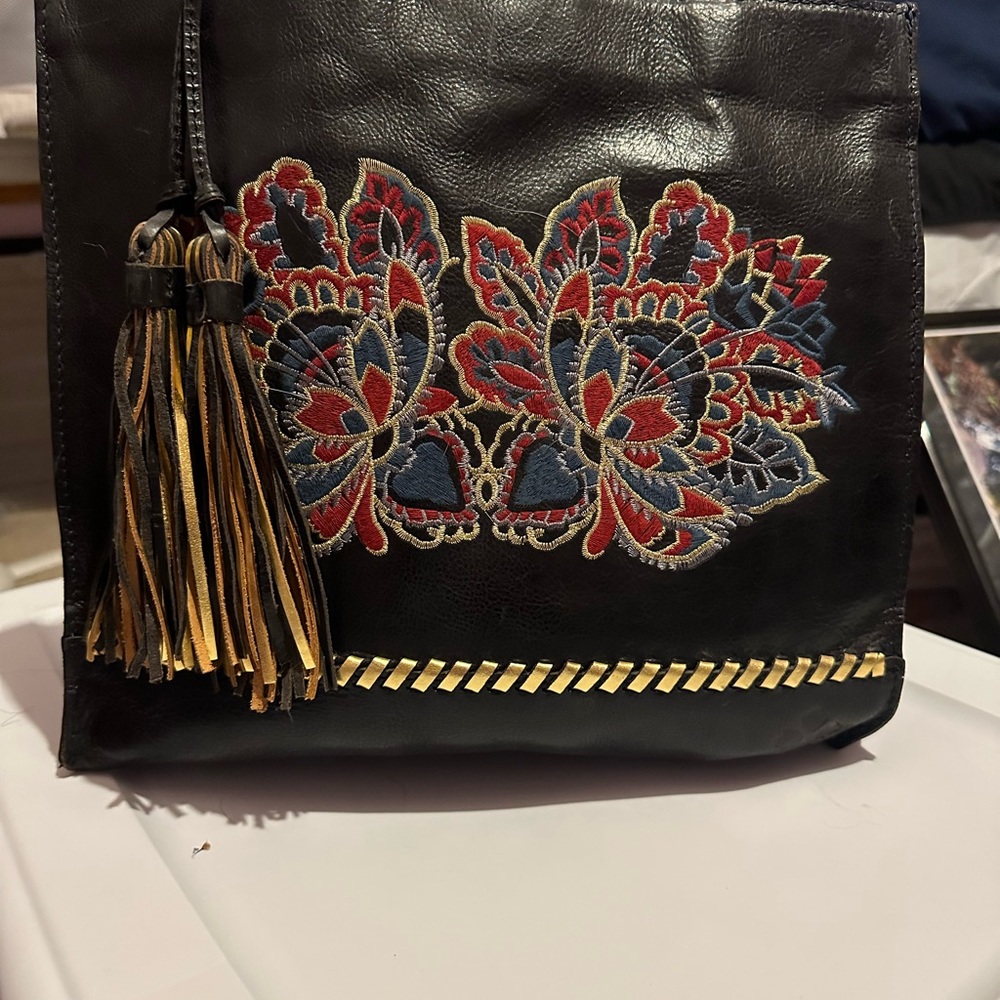 Black leather Patricia Nash handbag with tassels and floral pattern.